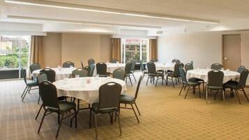A conference room with round tables and chairs, large windows with curtains, and a view of buildings outside.