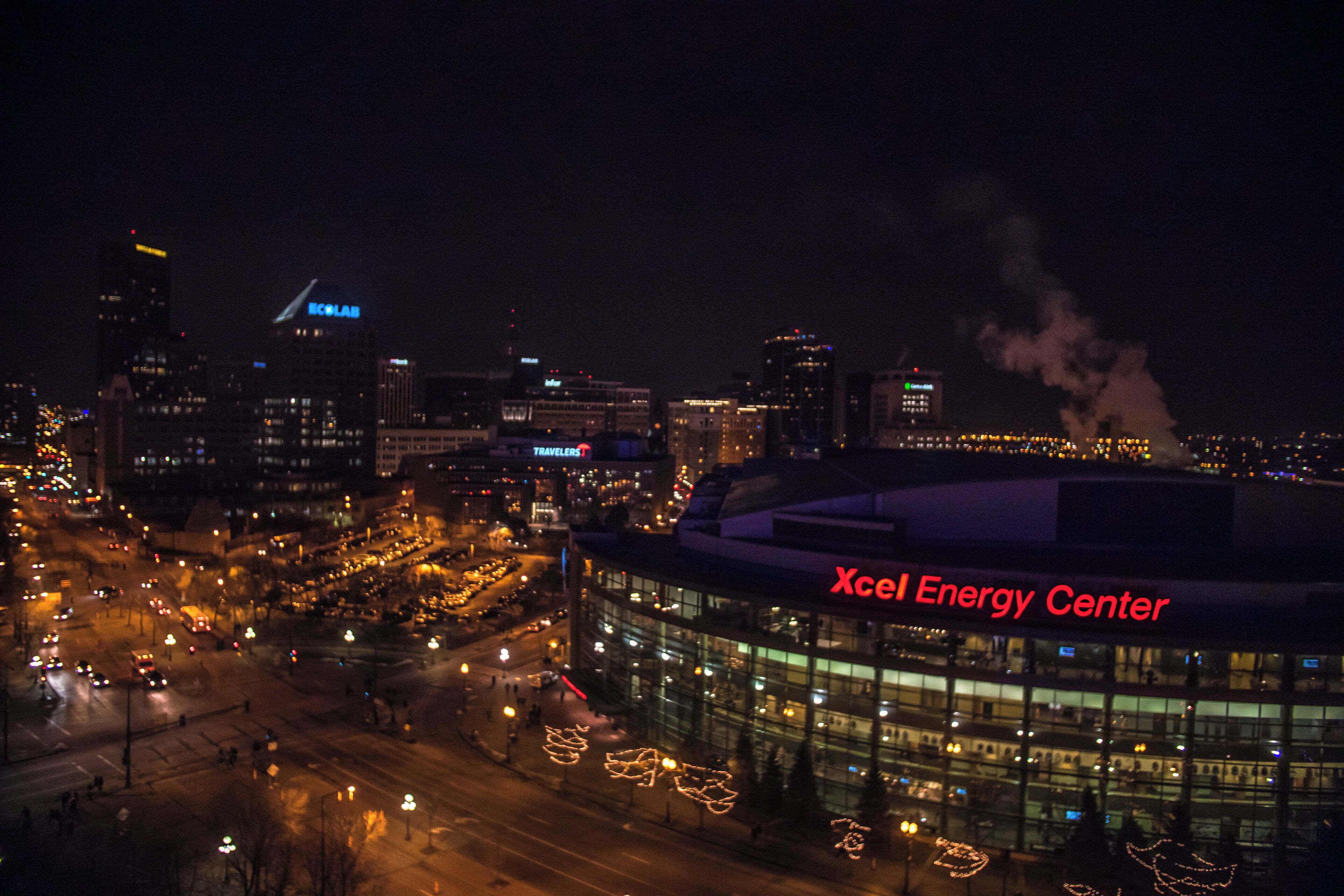 A nighttime cityscape with illuminated buildings and a prominent Xcel Energy Center.