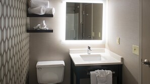 A bathroom with a toilet, sink, and mirror. There are towels on a shelf above the toilet. - Holiday Inn St. Paul Downtown by IHG (St. Paul)