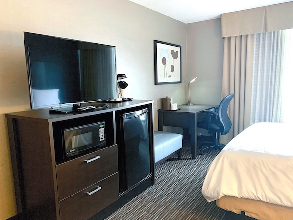 A hotel room with a bed, a desk with a chair, a television, a microwave, and a coffee machine.