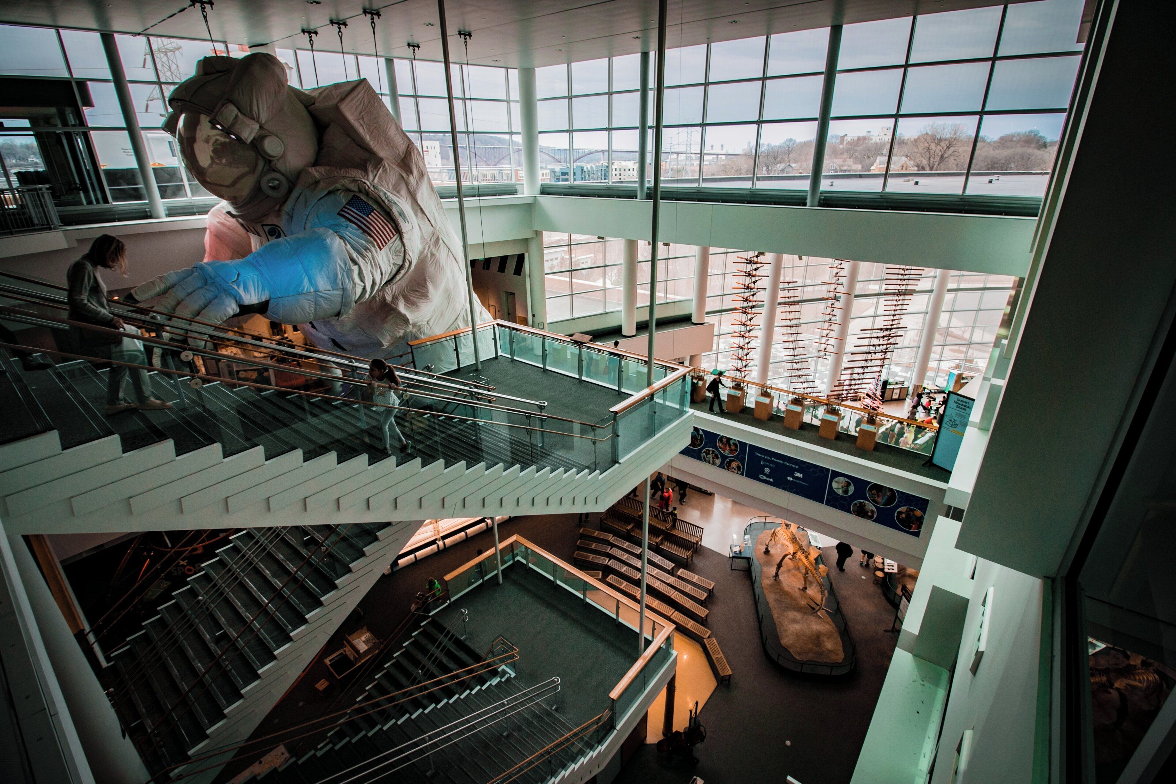 A multi-level atrium with a large sculpture, glass railings, and a view of the outside.