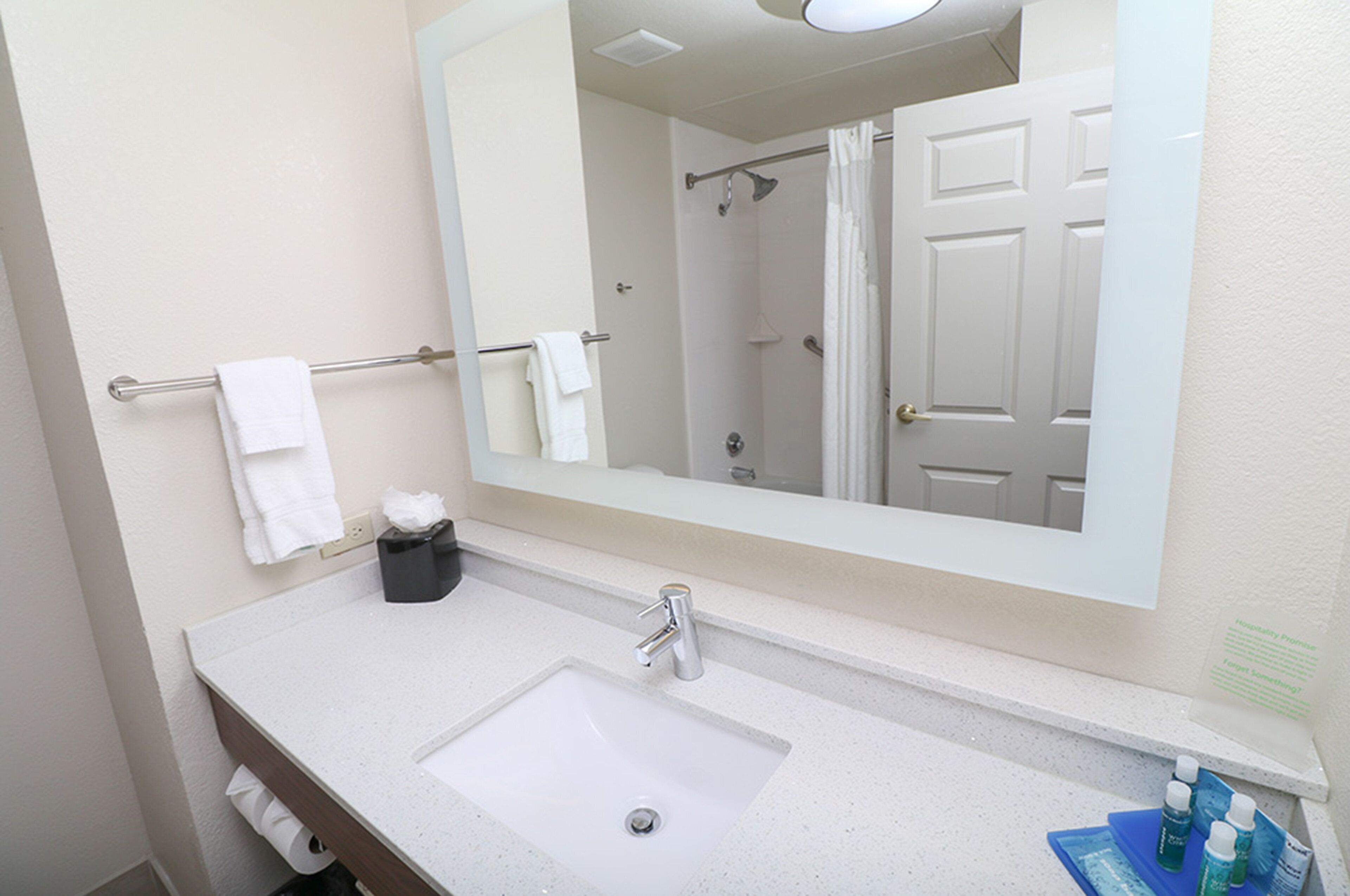 A bathroom with a white sink, a mirror, a towel rack with two white towels, a black tissue box, and a shower curtain.