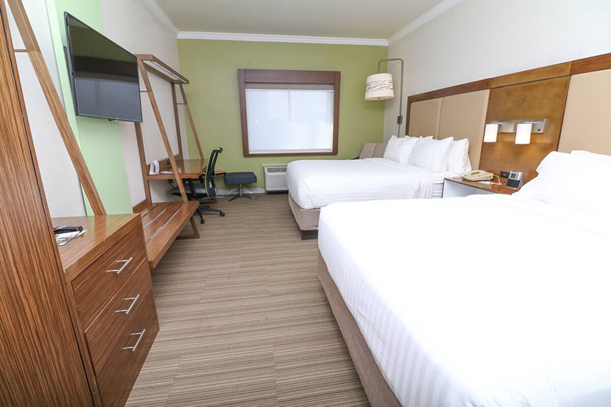 A hotel room with two beds, a TV, a desk with a chair, and a window.