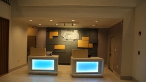 A reception area with two illuminated reception desks, a wall-mounted digital clock, and recessed ceiling lights.
