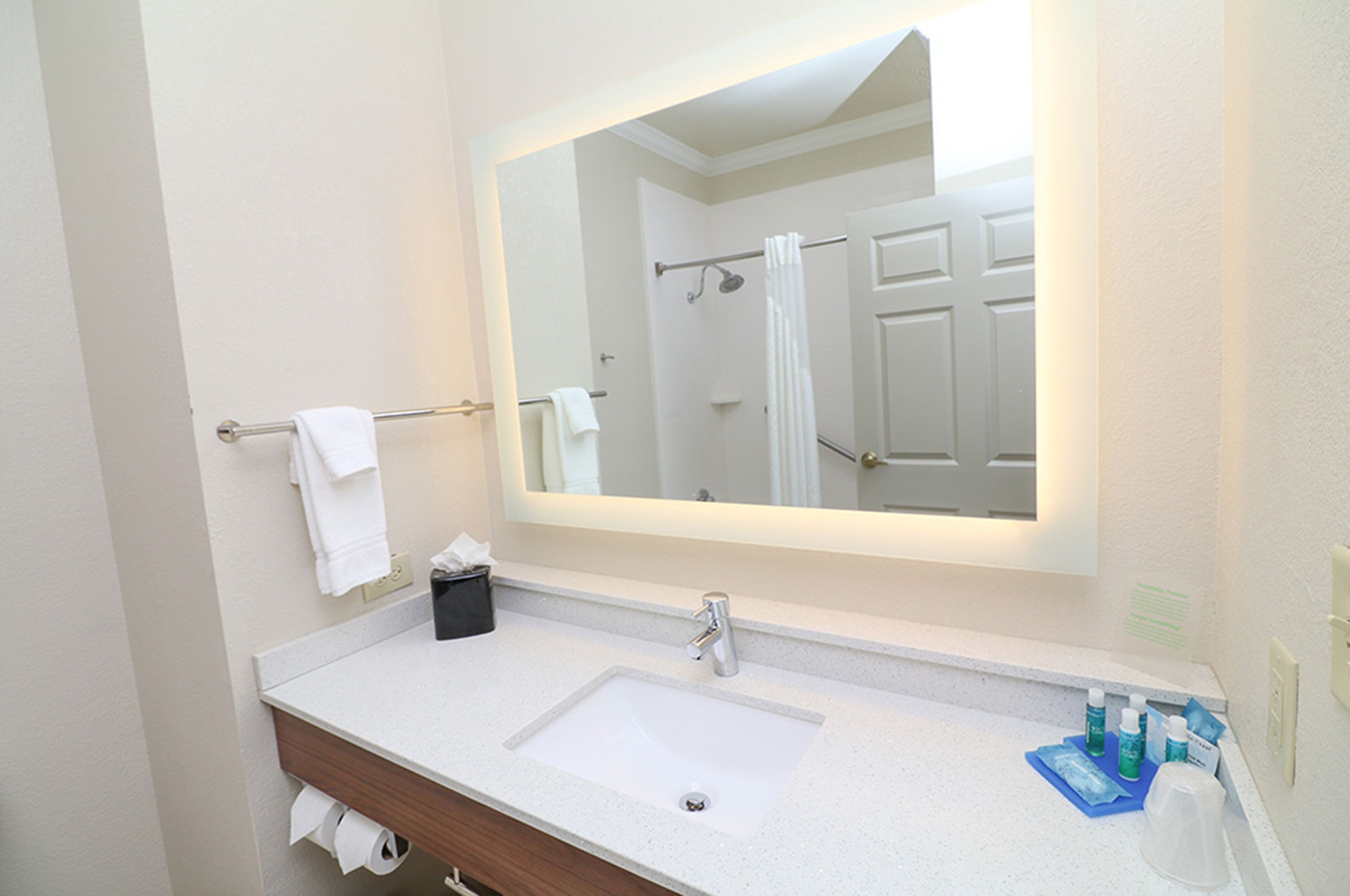 A bathroom with a white sink, a mirror, and a shower visible in the reflection.