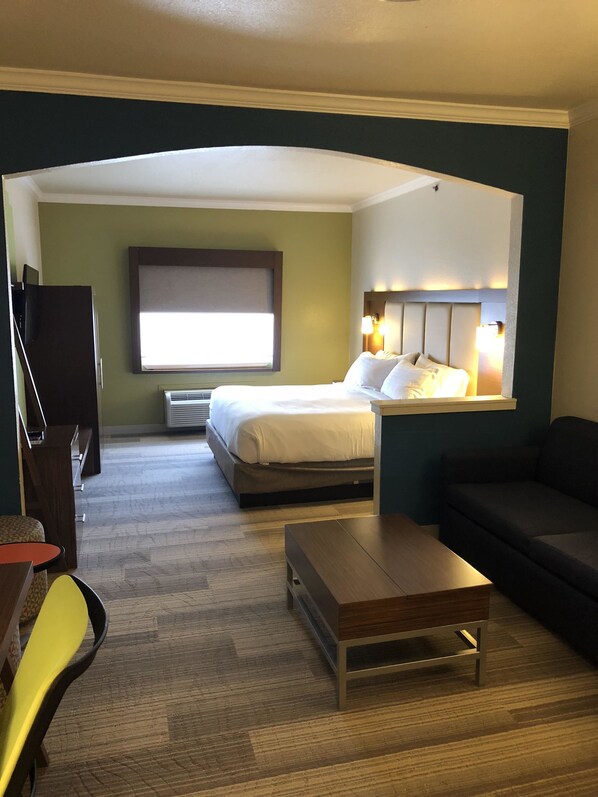 A hotel room with a bed, a sofa, a small table, a TV, and a window.