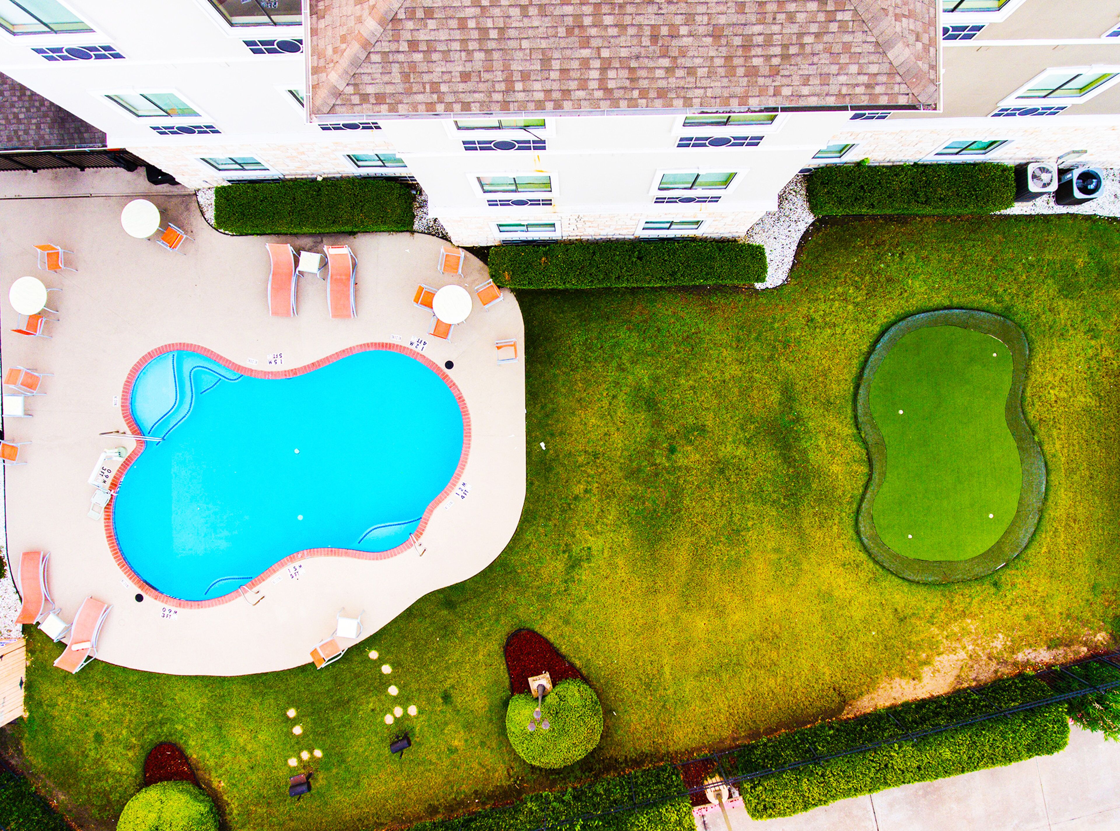 An aerial view of a swimming pool area with lounge chairs, a small pond, and well-manicured grass.