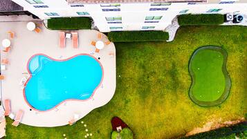 An aerial view of a swimming pool area with lounge chairs, a small pond, and well-manicured grass.