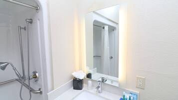 A bathroom with a shower, a sink, a mirror, and toiletries.