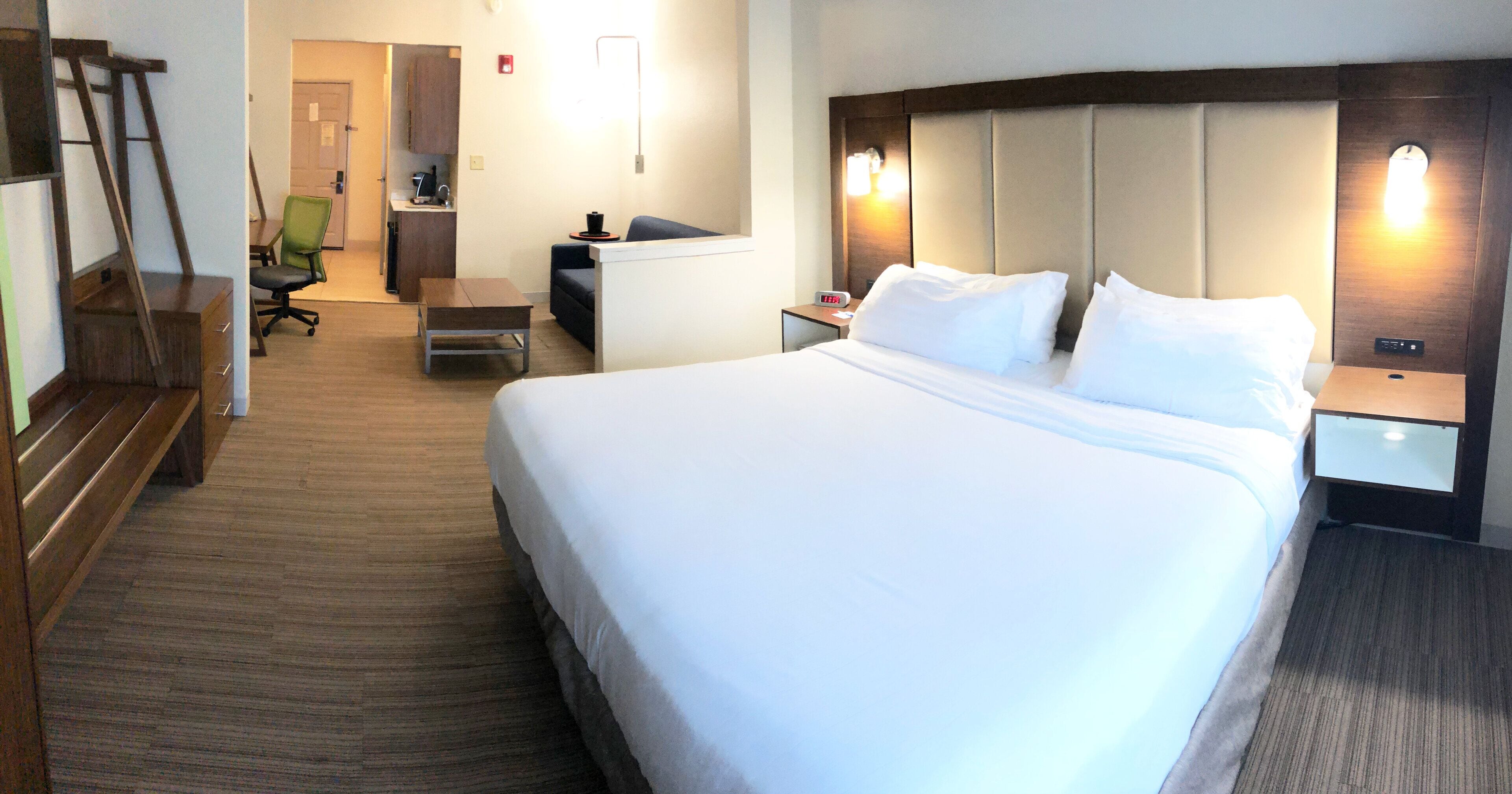 A hotel room with a large bed, a desk, a chair, and a small kitchenette.