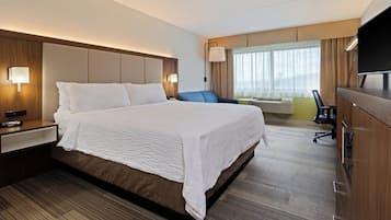 A hotel room with a large bed, a desk, a chair, a television, and a window with curtains.