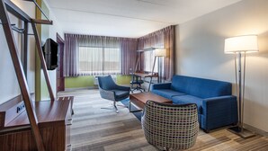 Una habitación de hotel moderna con un sofá azul, un escritorio de madera, una silla, una lámpara y un televisor.