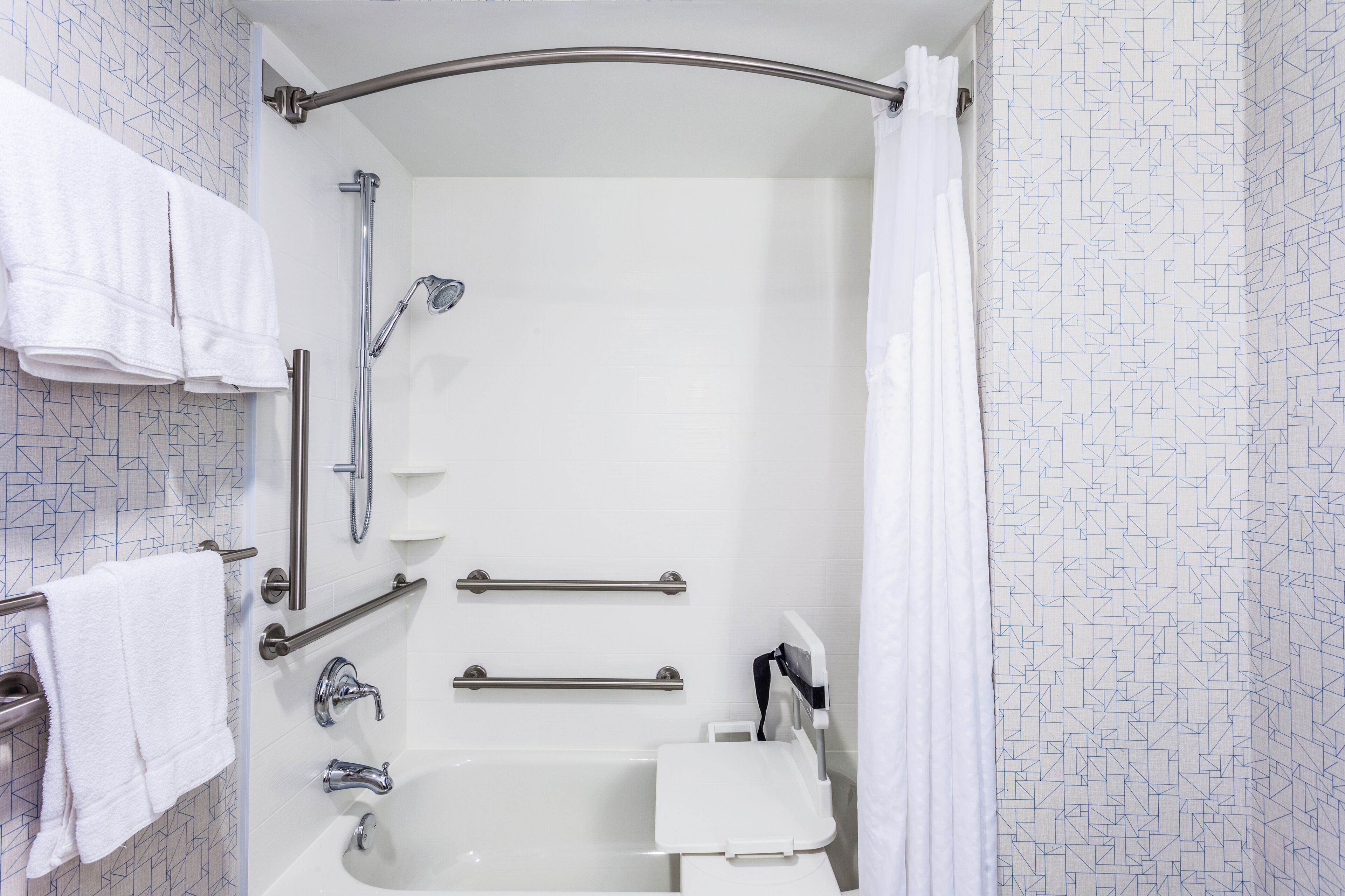 A modern bathroom with a walk-in shower, grab bars, a handheld showerhead, and a white sink with a mirror.