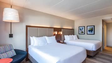 A hotel room with two beds, a sofa, a desk, and a lamp.