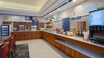 Uma área de café da manhã moderna com estação de autoatendimento, assentos e dispensador de água.