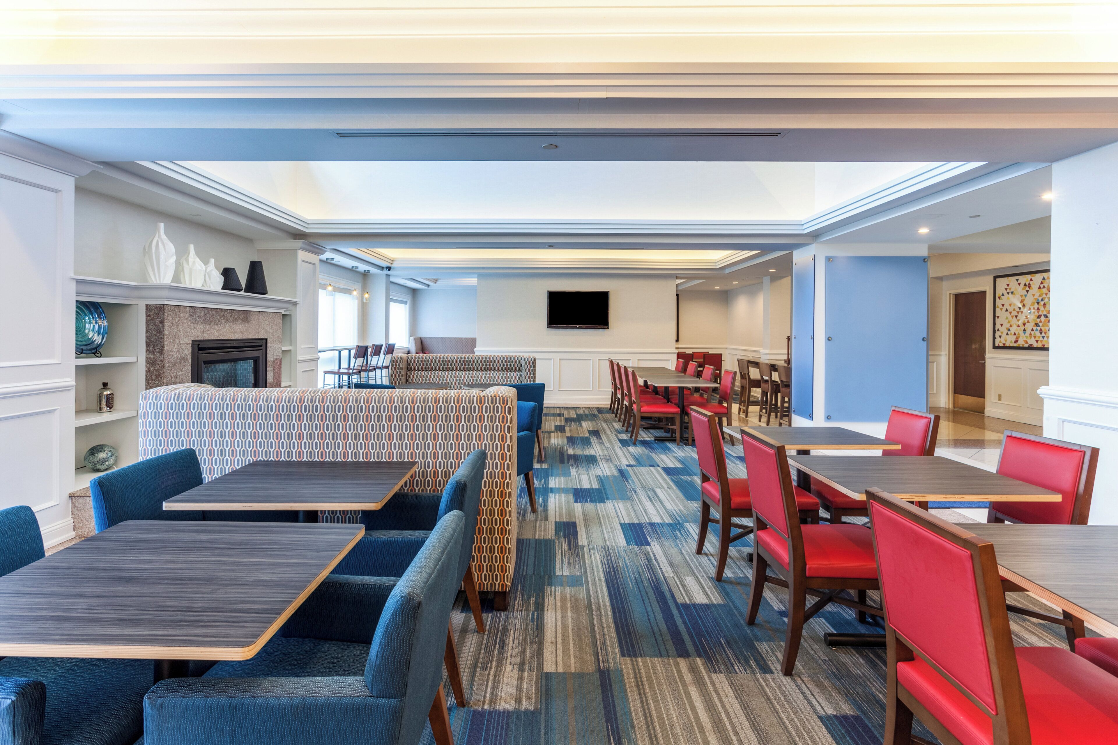 Un comedor de hotel con diversas opciones de asientos, incluyendo cabinas y mesas, una chimenea y un televisor de pantalla plana montado en la pared.