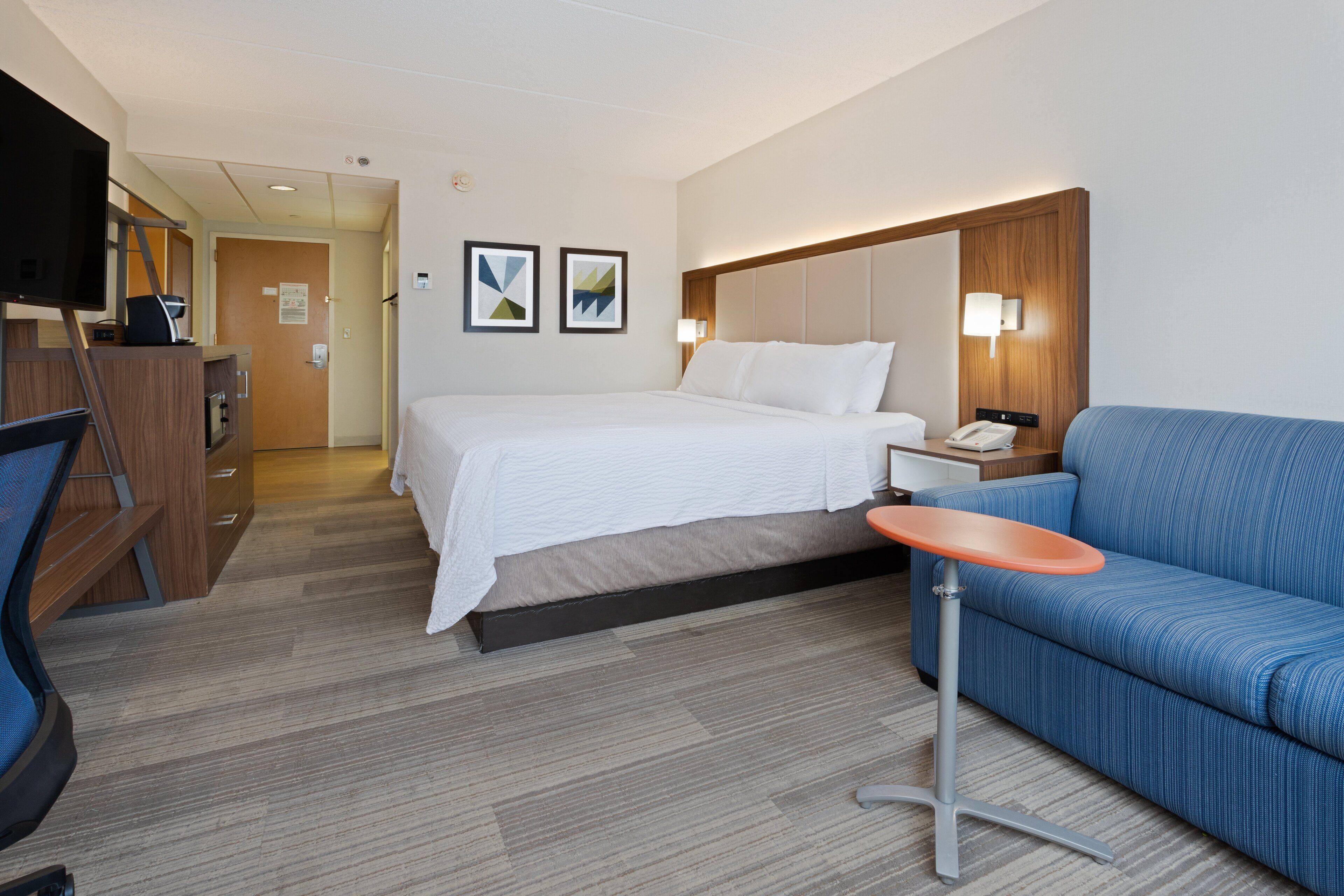 A hotel room with a bed, a blue sofa, a desk with a telephone, and a TV.