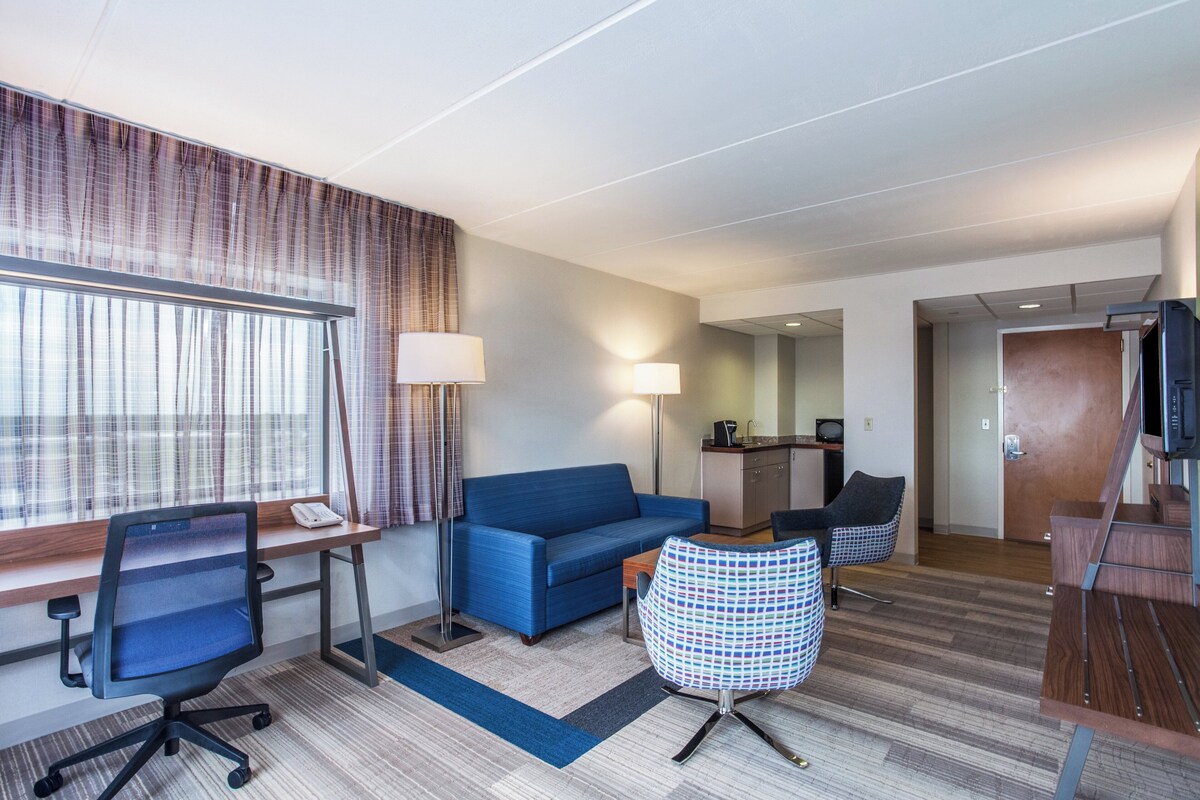 A hotel room with a desk, office chair, sofa, round table, and a television.
