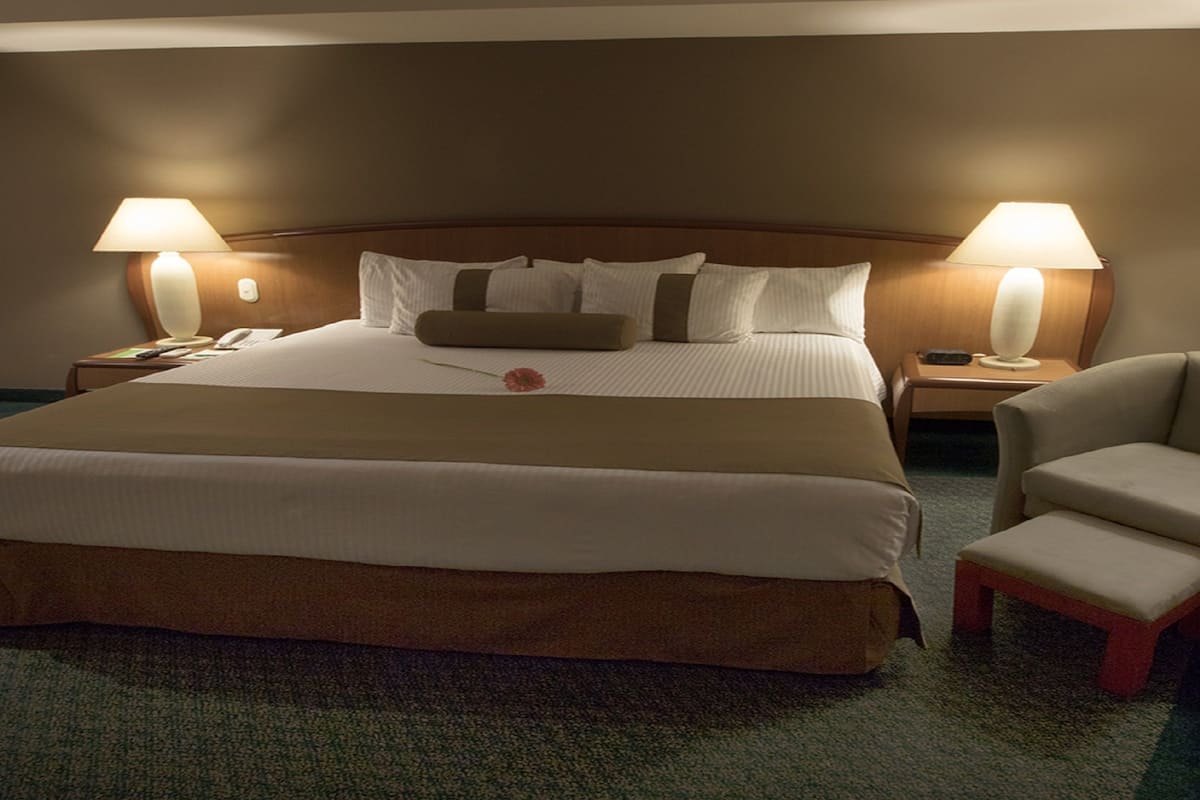 Una habitación de hotel con una cama grande, dos mesitas de noche, una silla y dos lámparas.