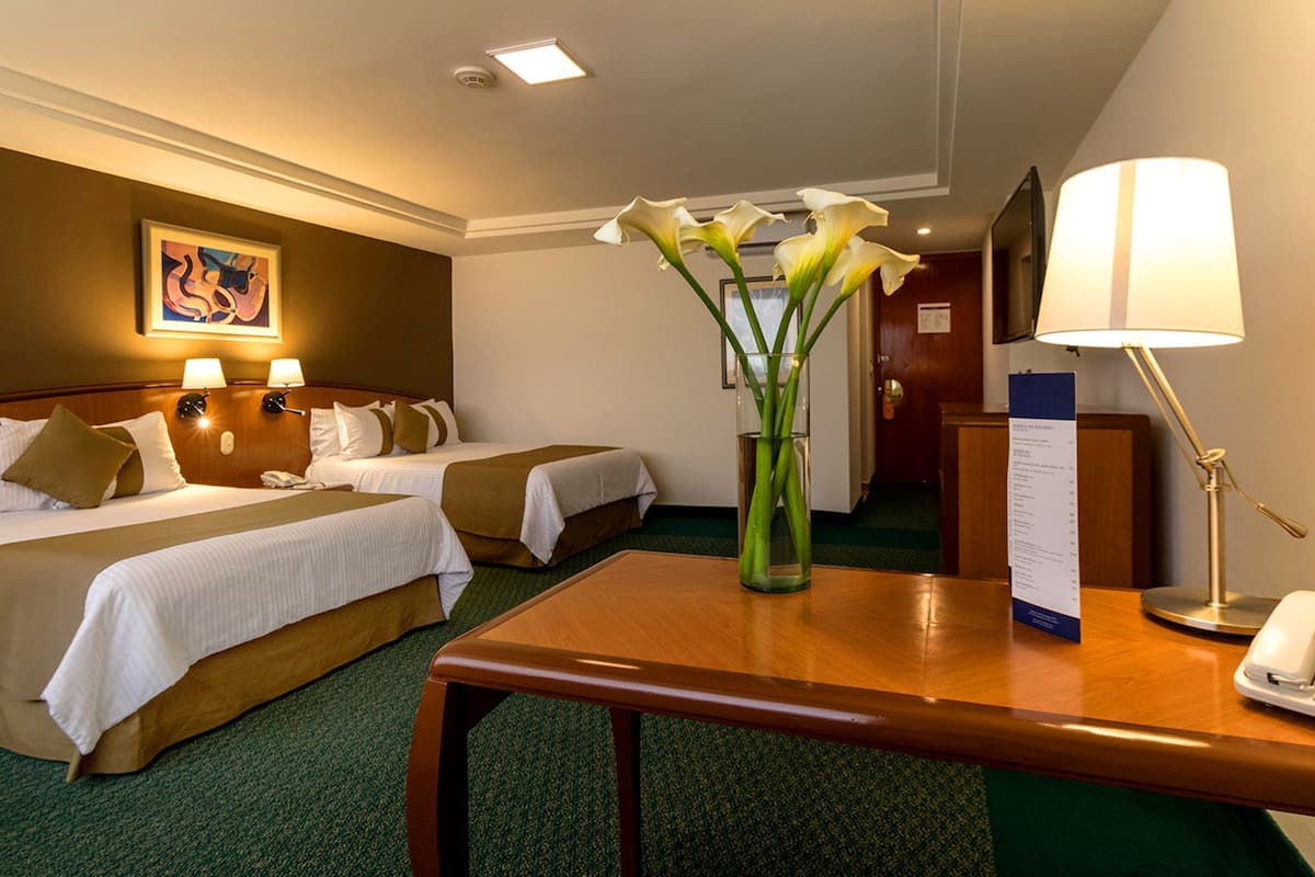 Habitación de hotel con dos camas, un escritorio con teléfono, un jarrón con flores y una lámpara.