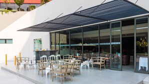 An outdoor cafe with wooden tables and chairs, a glass entrance, and a modern building facade. - Hotel Misión Toreo Centro De Convenciones (Naucalpan)