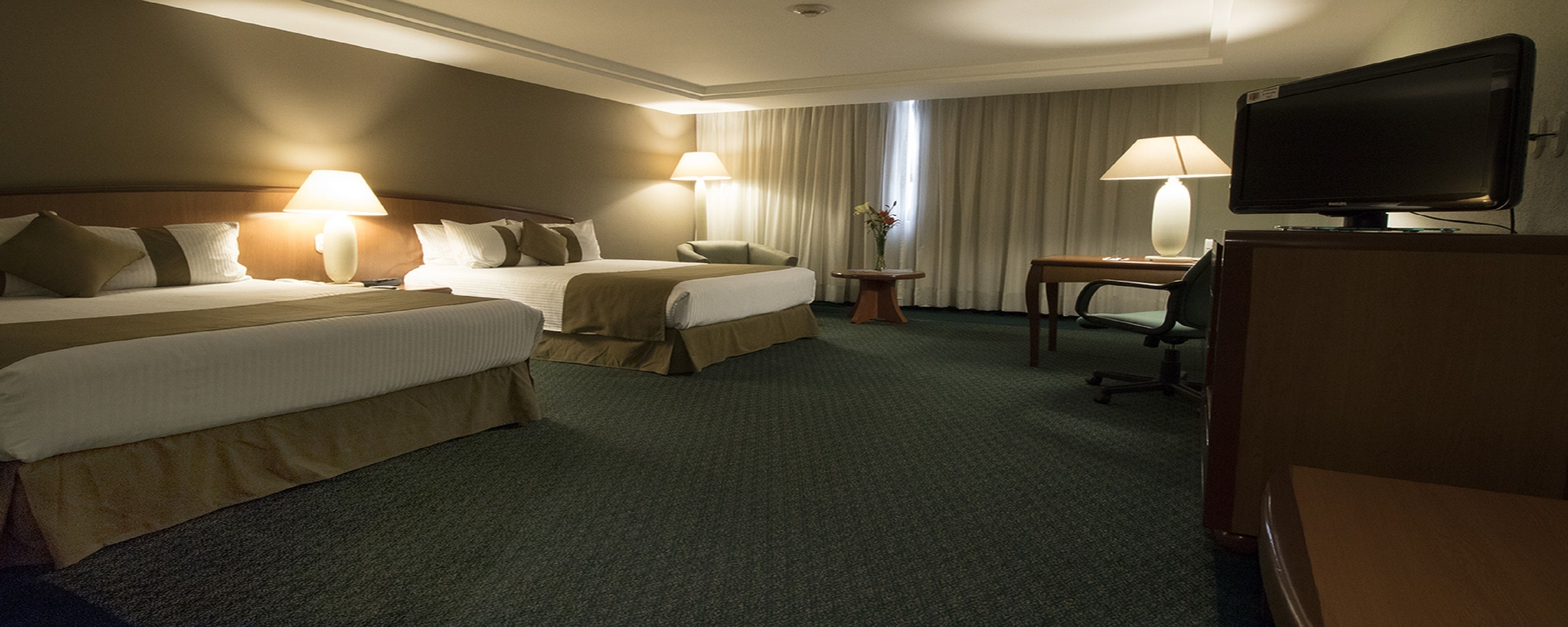 A hotel room with two beds, a desk, a television, and a chair.