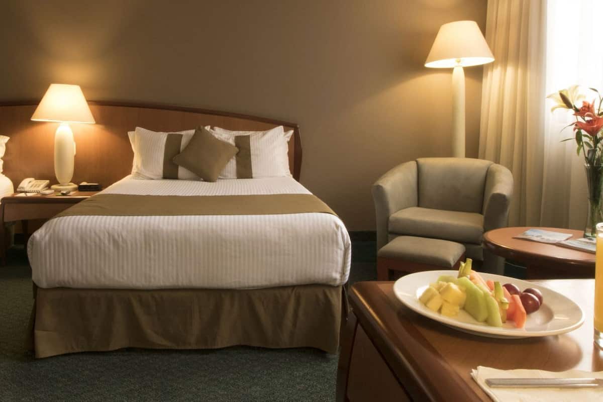 Une chambre d’hôtel avec deux lits, un bureau sur lequel se trouve une assiette de fruits et un verre de jus, une chaise et une lampe.