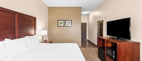 Una habitación de hotel con una cama grande, un televisor sobre un soporte de madera y un pequeño escritorio con una lámpara.