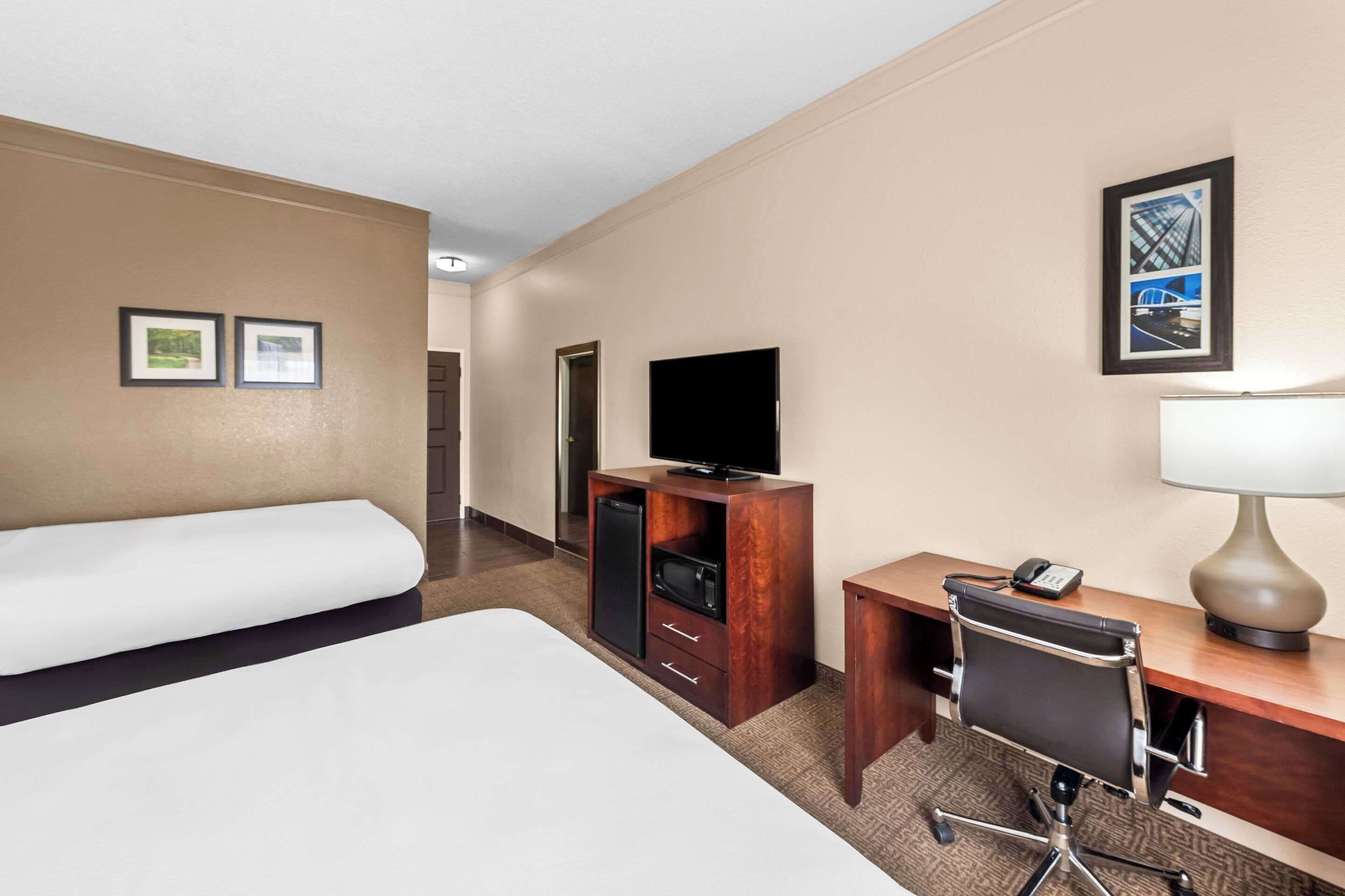 A hotel room with a bed, a desk with a lamp, a chair, a television, and a small cabinet.