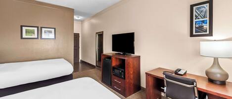 A hotel room with a bed, a desk with a lamp, a chair, a television, and a small cabinet.