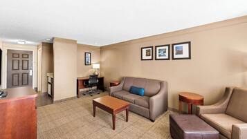 A hotel room with a sofa, armchair, wooden coffee table, and a desk with a lamp.