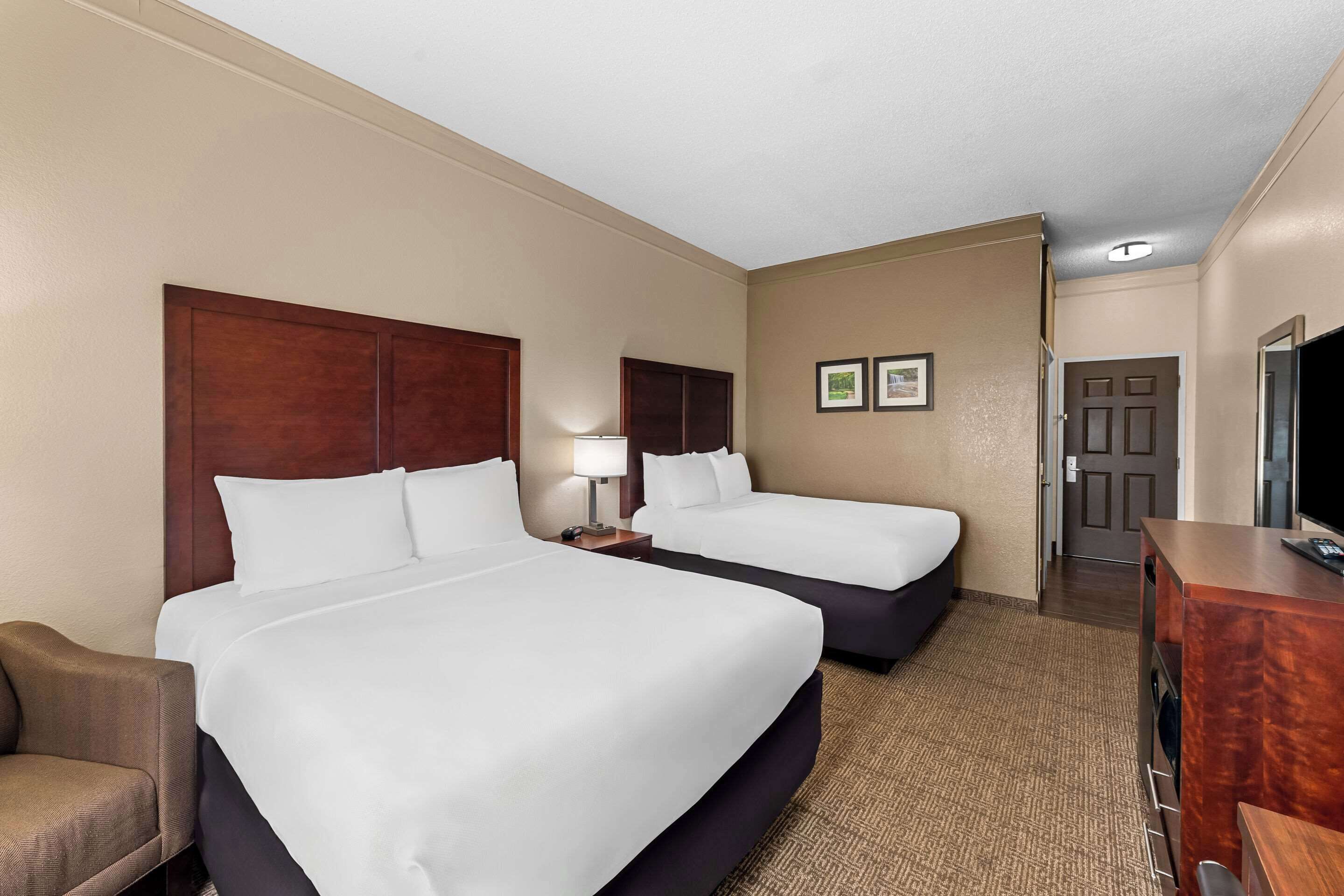 A hotel room with two beds, a desk, a chair, and a television.