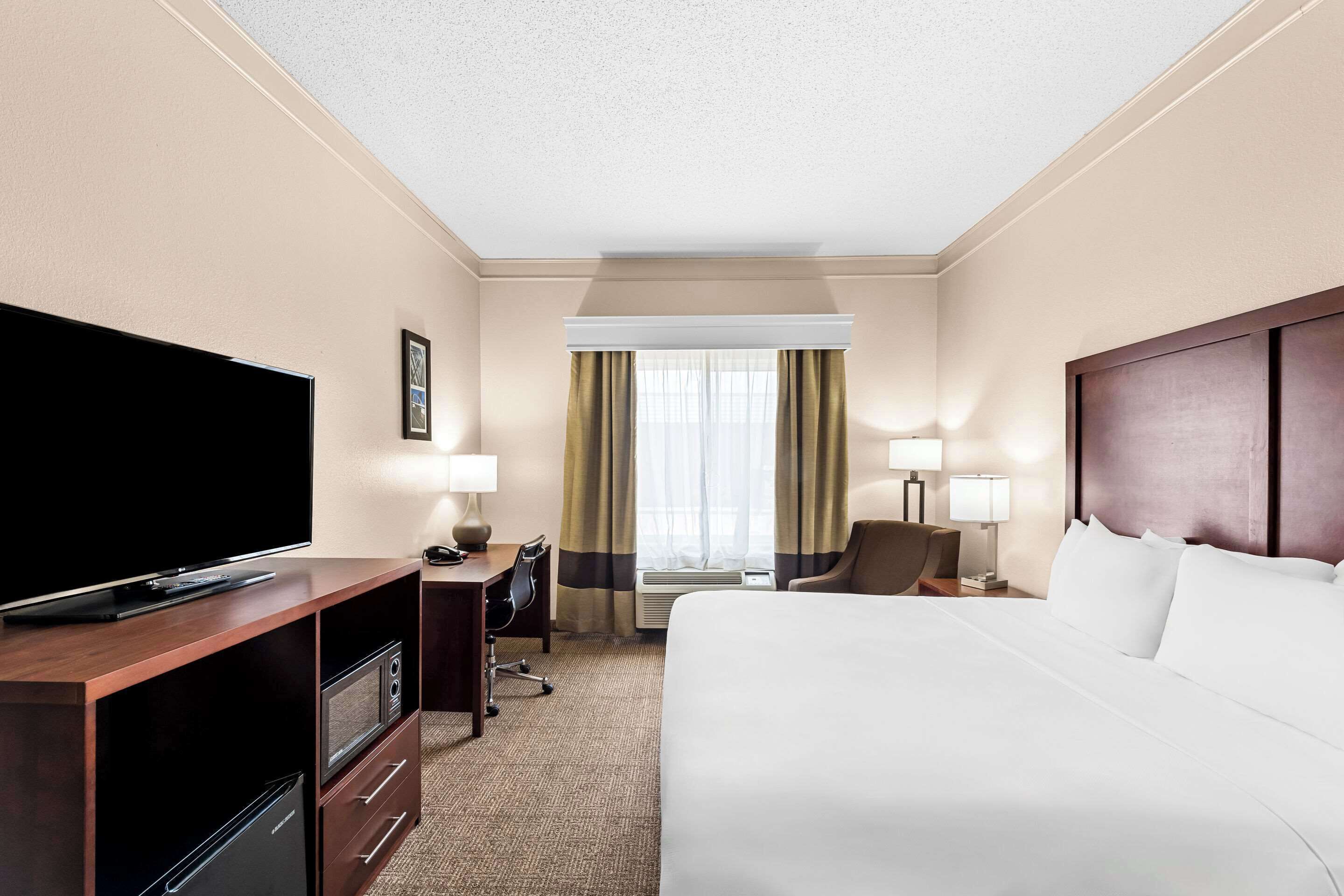 A hotel room with a bed, a TV, a desk, a chair, and a window with curtains.