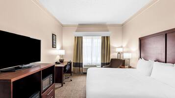 A hotel room with a bed, a TV, a desk, a chair, and a window with curtains.