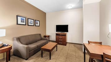 Ein Hotelzimmer mit einer Couch, einem Fernseher, einem Holztisch und einem kleinen Schrank.