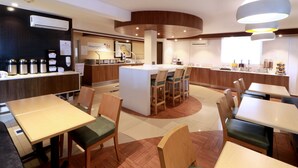 Un intérieur de restaurant moderne avec un îlot central, des places assises au bar et un comptoir équipé de machines à café.