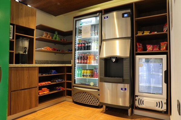 A kitchen with a refrigerator, a freezer, and shelves stocked with snacks and beverages.