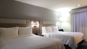 Une chambre d’hôtel avec deux lits, une table de chevet, une lampe fixée au mur et une fenêtre avec des rideaux.