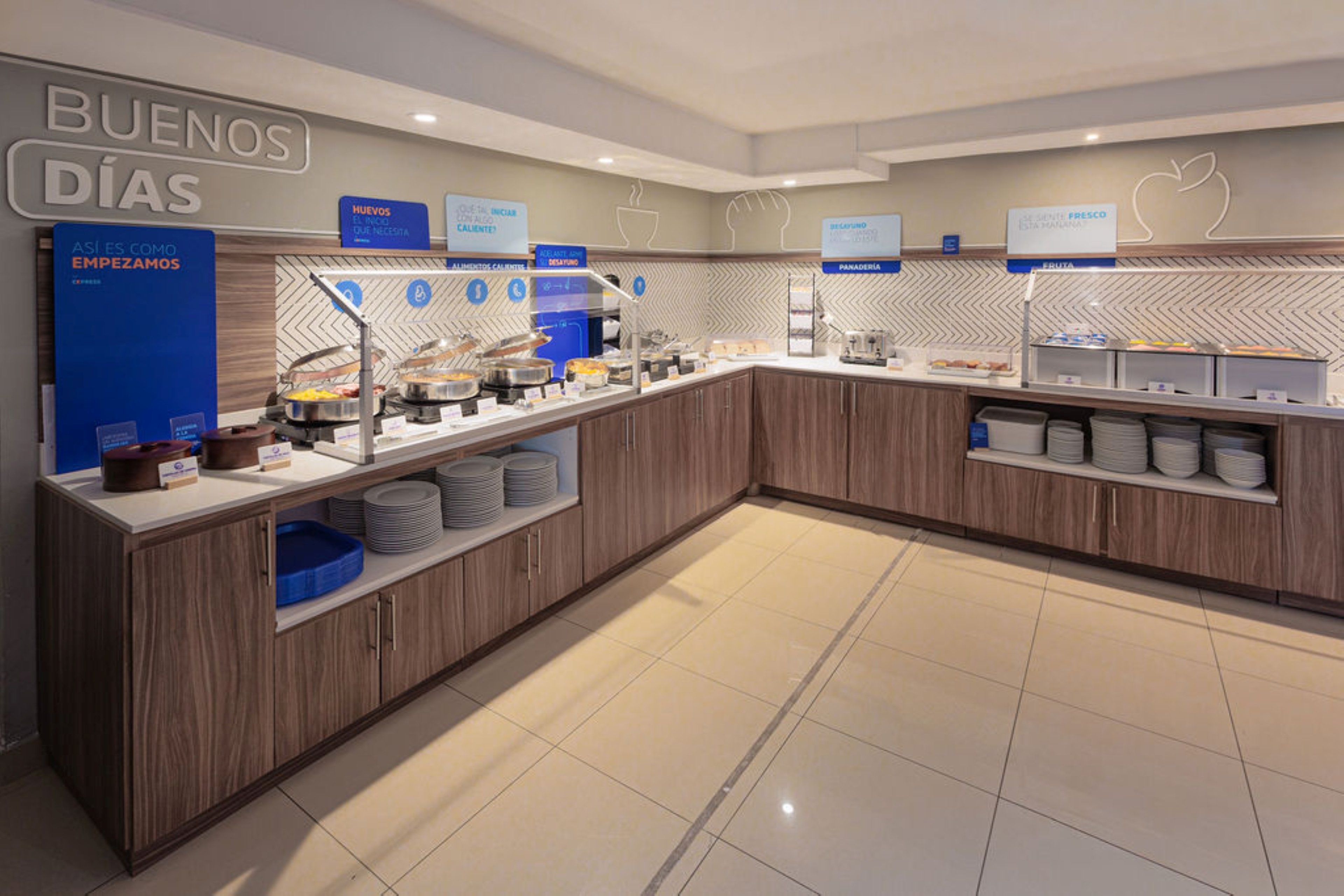 A breakfast buffet area with labeled food stations, including a fruit section and a panaderia.