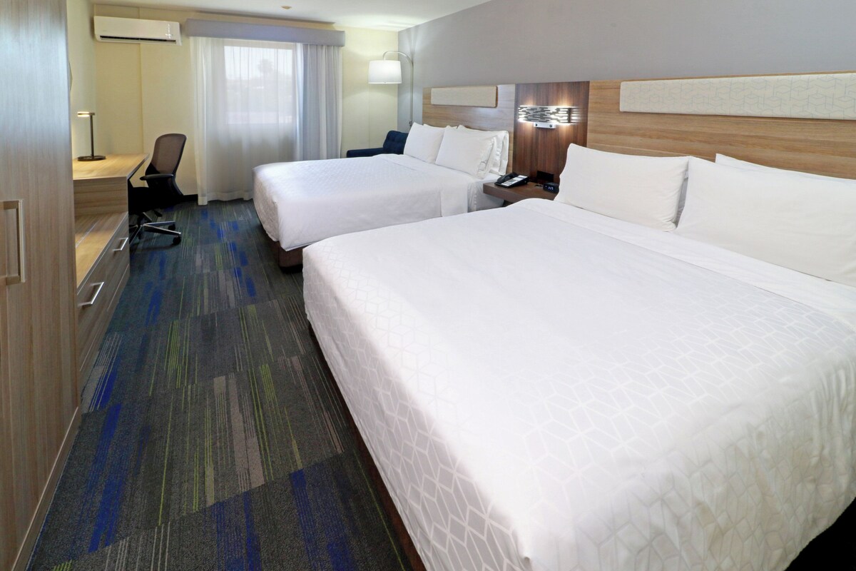 Una habitación de hotel con dos camas, un escritorio, una silla, una lámpara y una ventana con cortinas.