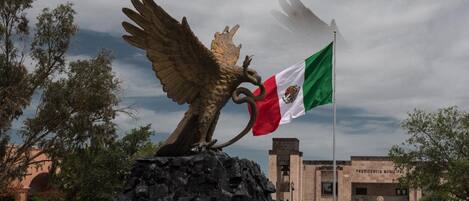A statue of an eagle with a flag on its back, set on a rocky base, with a building in the background.