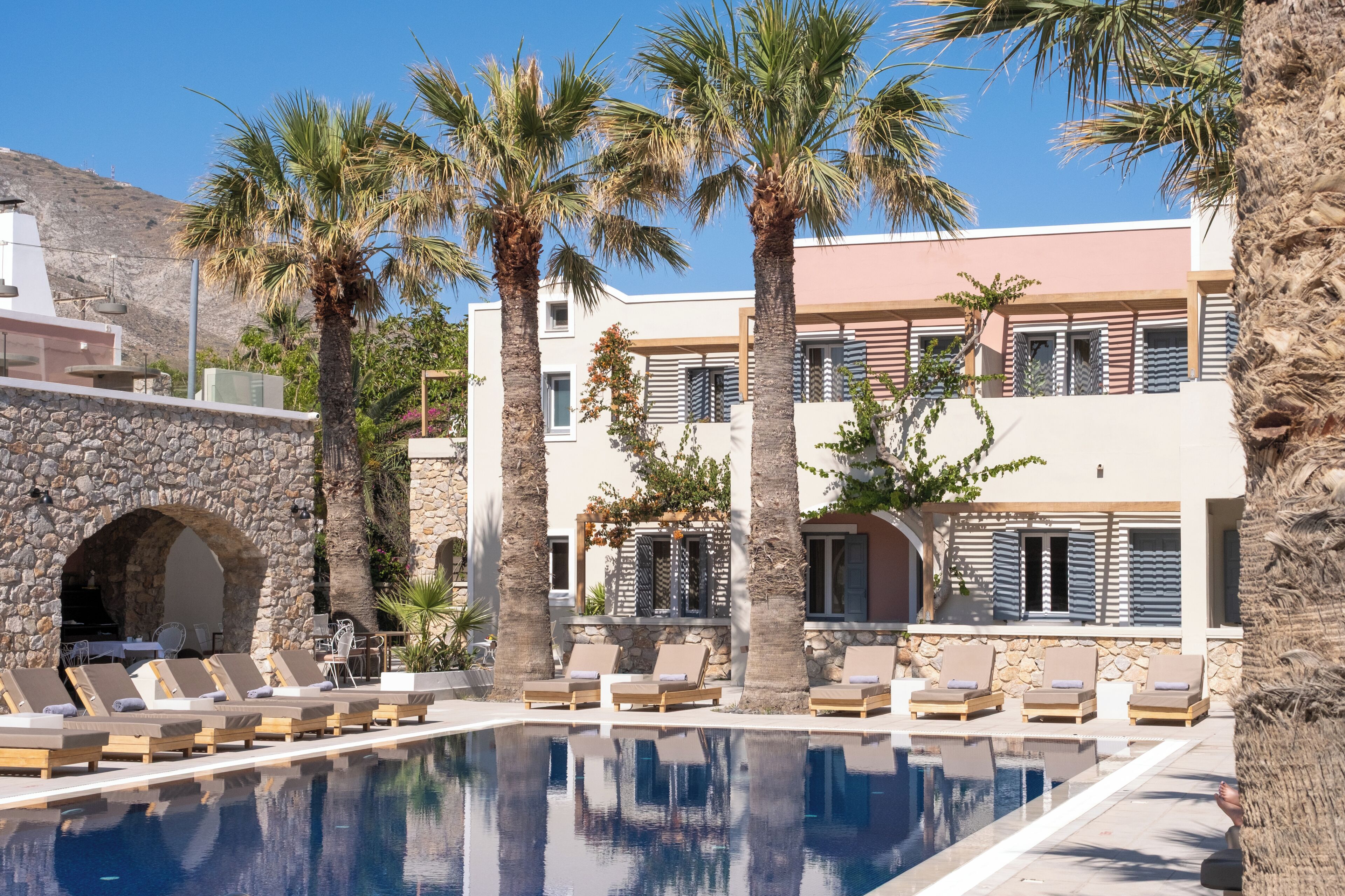A poolside area with lounge chairs, a stone wall, and a building with multiple balconies and windows.