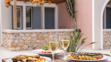 Un espace de restauration en plein air, avec un mur en pierre, une table dressée avec des assiettes remplies de nourriture et deux verres de vin blanc.