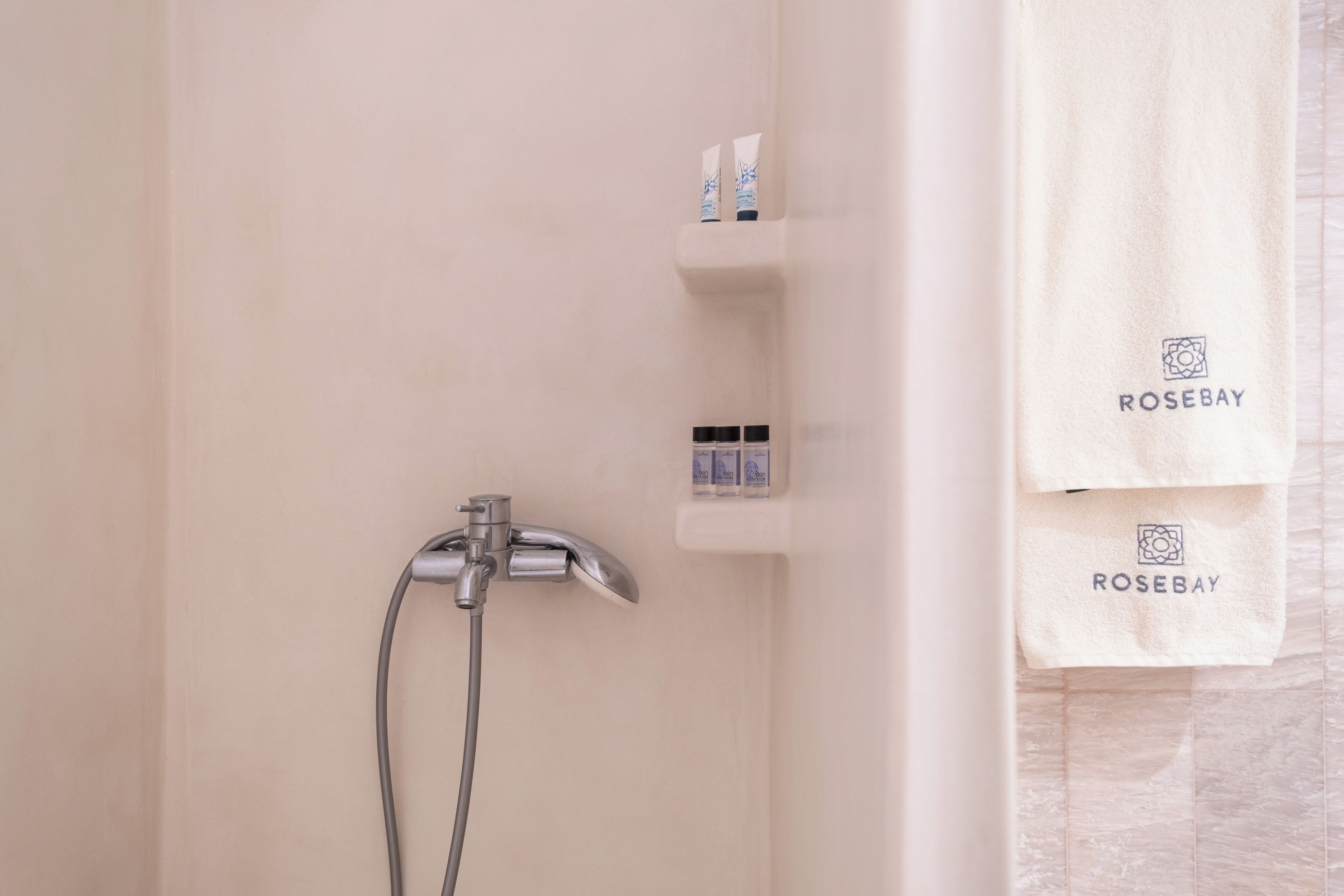 A bathroom with a shower, a towel rack with towels, and a shelf with toiletries.