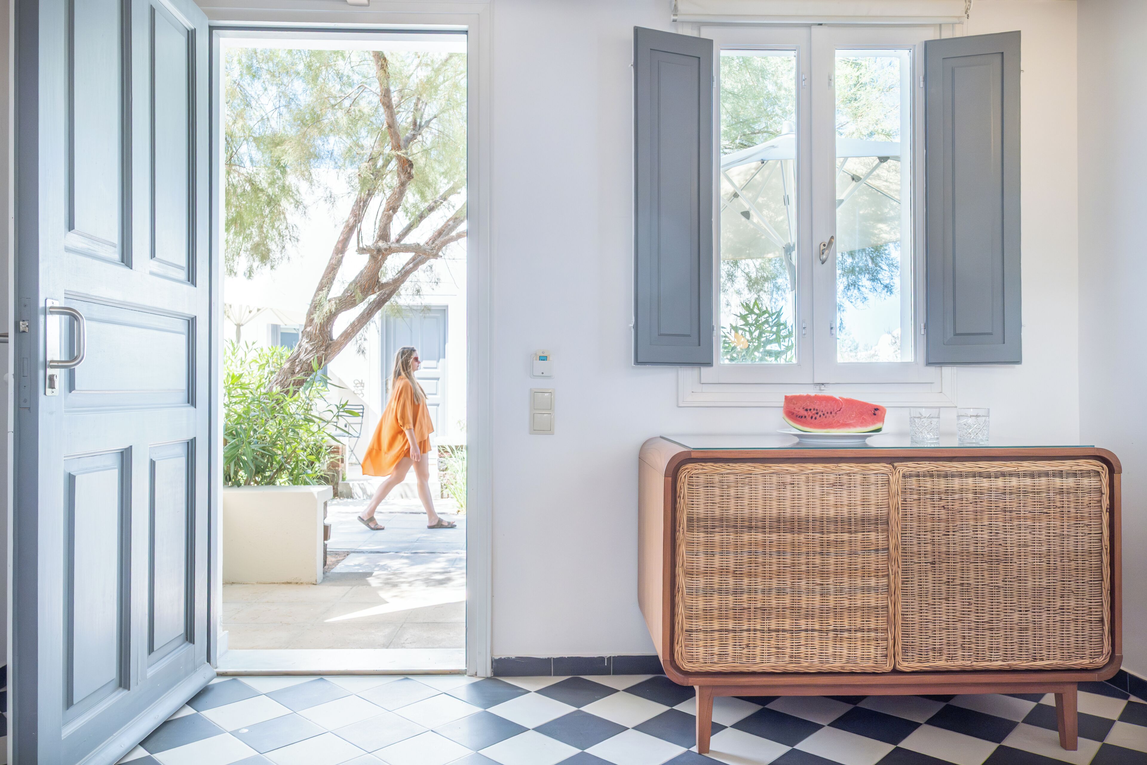 A room with a checkered floor, a wicker chair, and a door leading outside.