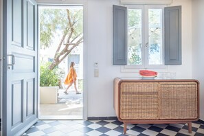 A room with a checkered floor, a wicker chair, and a door leading outside. - Rosebay Hotel (Santorini)