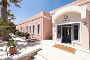 A building with a pink facade, a sign reading 'ROSE BAY', and a door with a window. - Rosebay Hotel (Santorini)