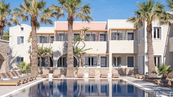 A pool area with lounge chairs, palm trees, and a building with multiple windows and shutters.