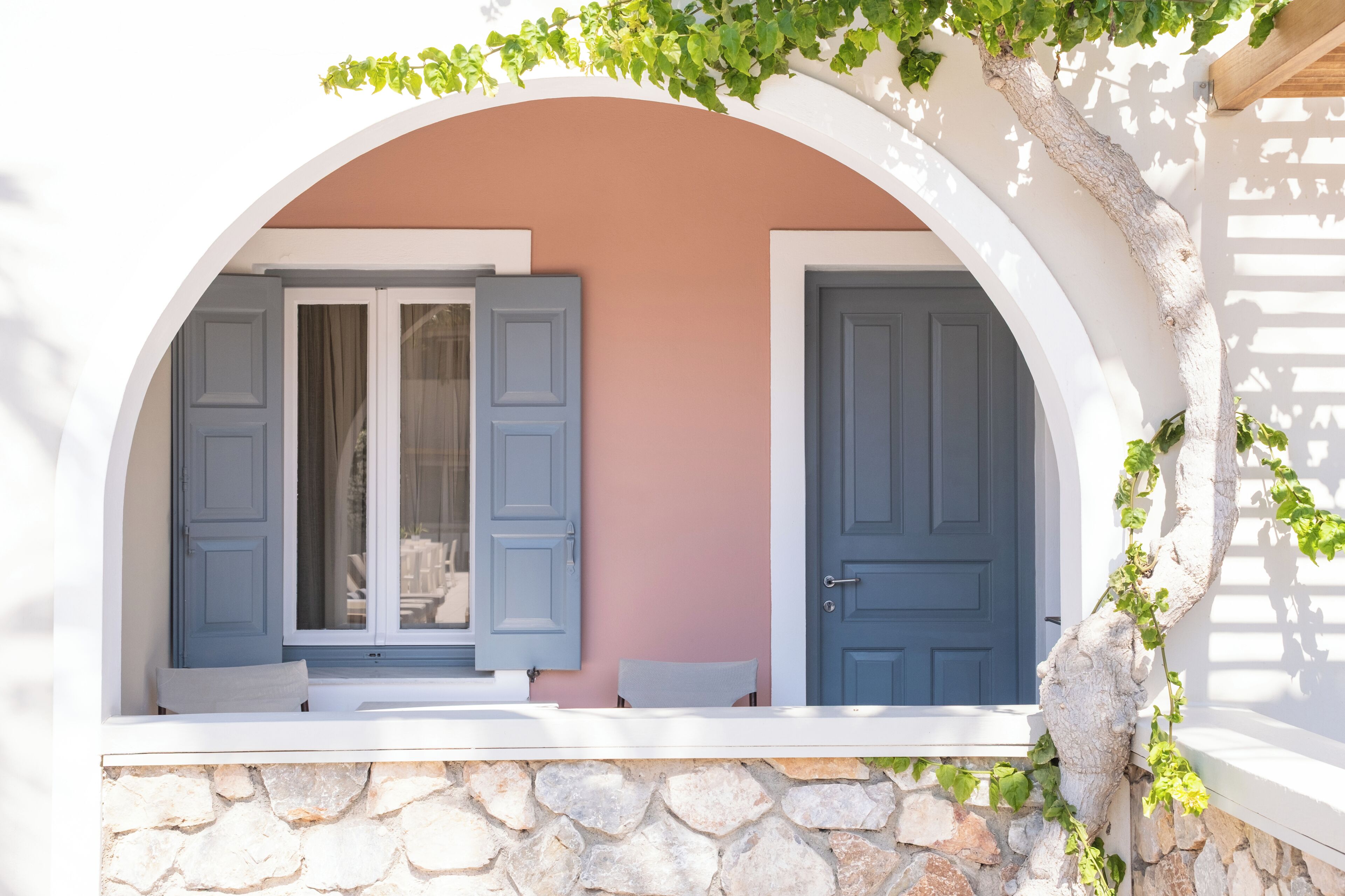 A stone wall with a window and a door, both with shutters.