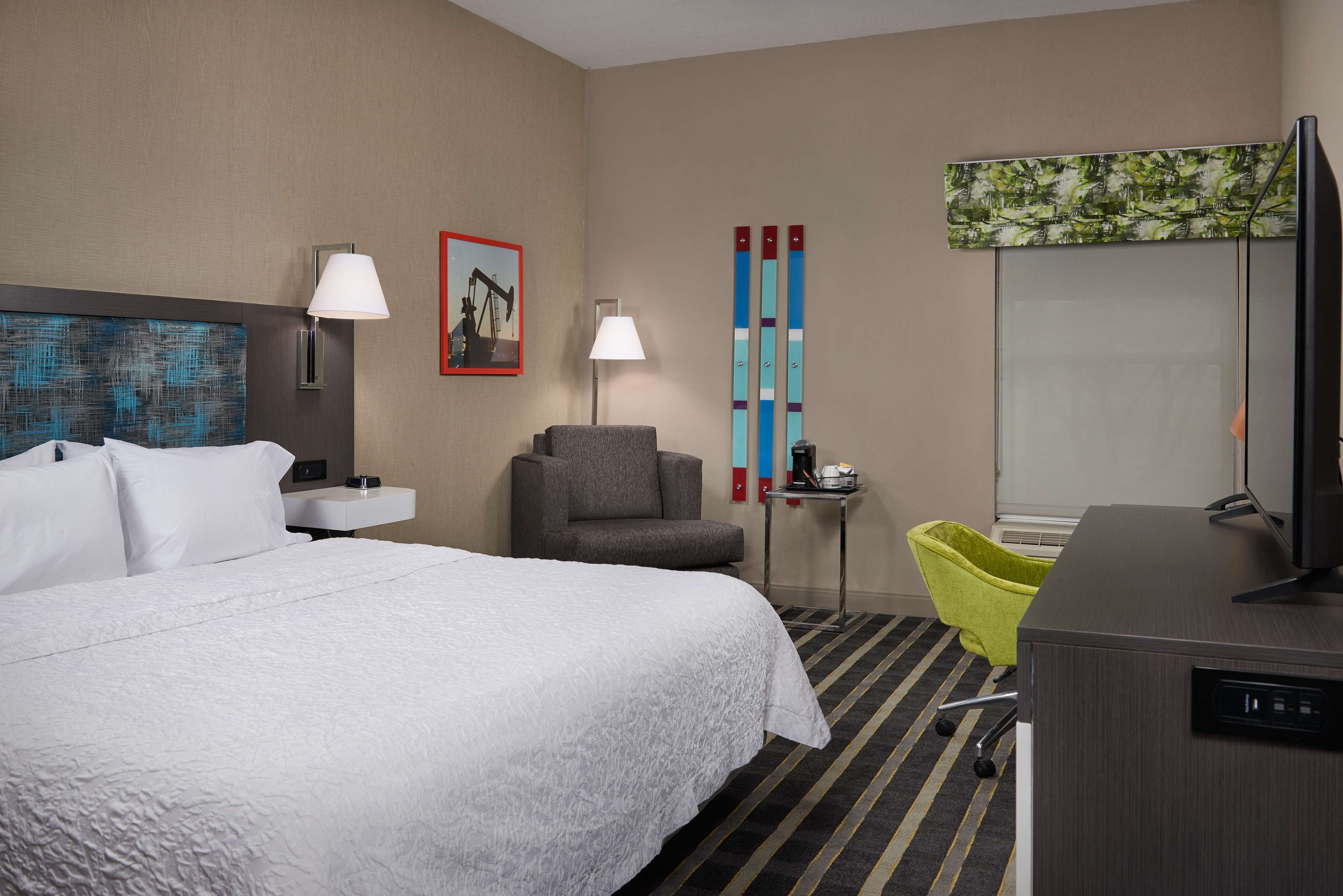 Habitación de hotel con una cama grande, un escritorio, una silla, un televisor y un cuadro en la pared.